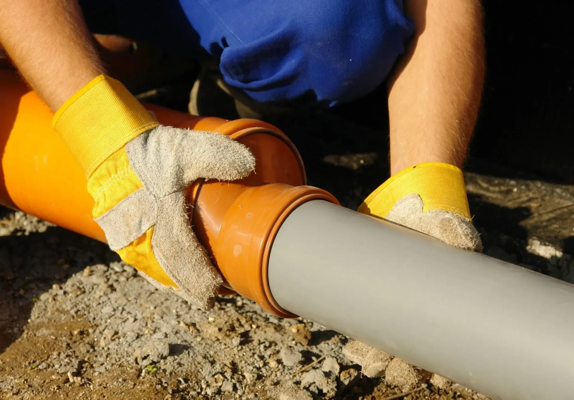 A person in yellow gloves is fixing a pipe.