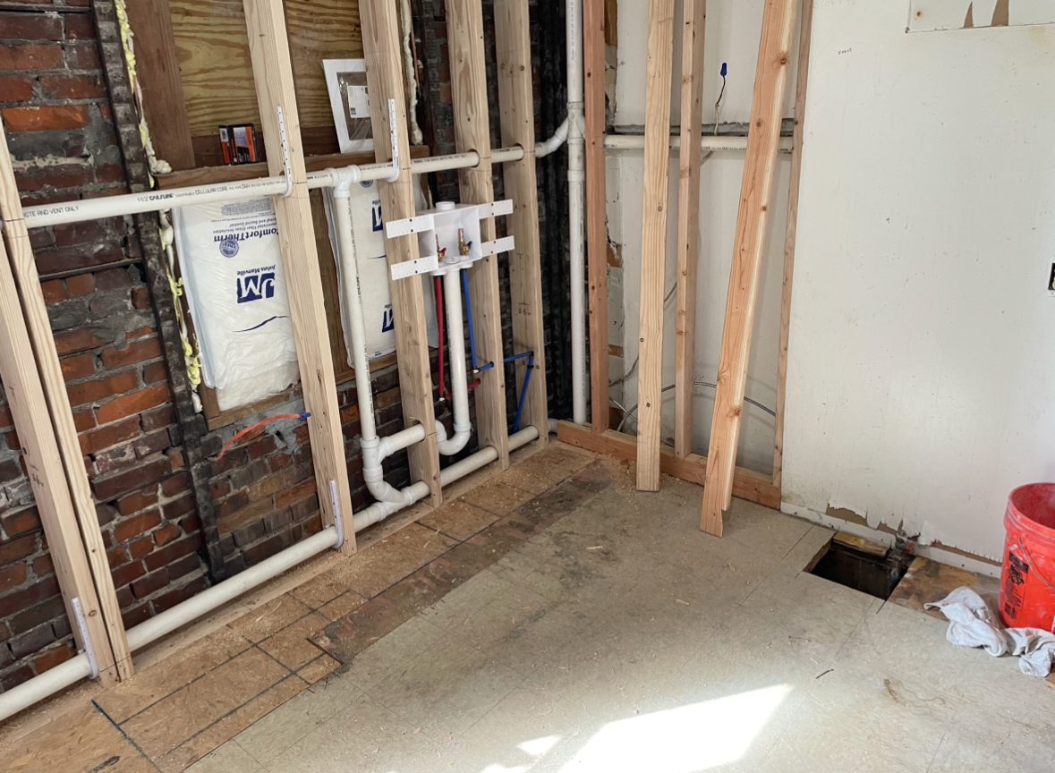 A bathroom with exposed pipes and walls in the process of being remodeled.